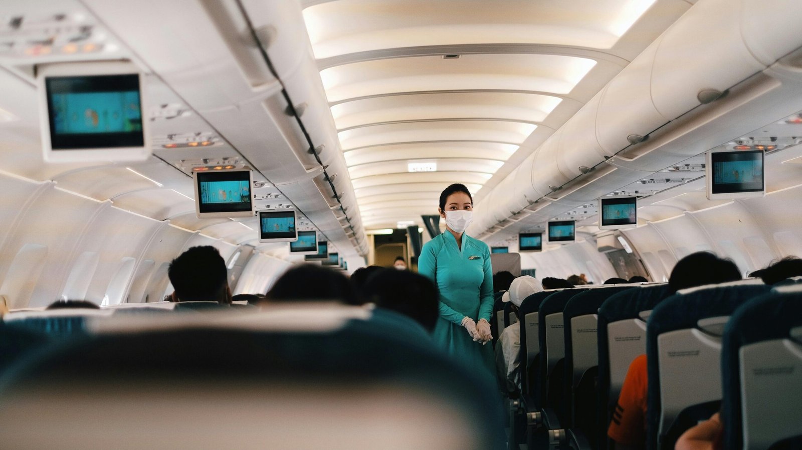 Flight attendant wearing a face mask attending to passengers in an airplane cabin.